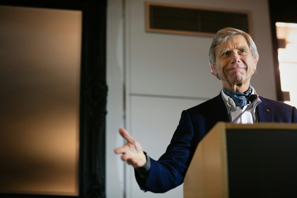 Hermann Hauser addressing a crowd from a lectern. His arms are outstretched as he gesticulates while speaking.