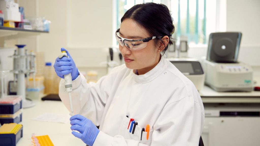 Constructive Bio staff member in a white lab coat and gloves working in the lab with apparatus.