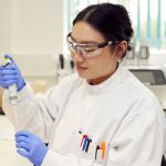 Constructive Bio staff member in a white lab coat and gloves working in the lab with apparatus.