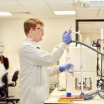 A Constructive Bio team members working in the laboratory, wearing a white lab coat and gloves while using apparatus.