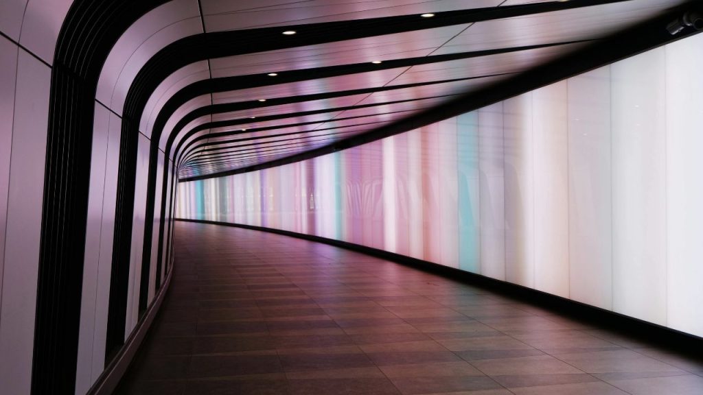 An empty walkway tunnel in a transport system with a wall lit on one side. The image represents Cryptosense technology which was used to secure data across applications and infrastructure.
