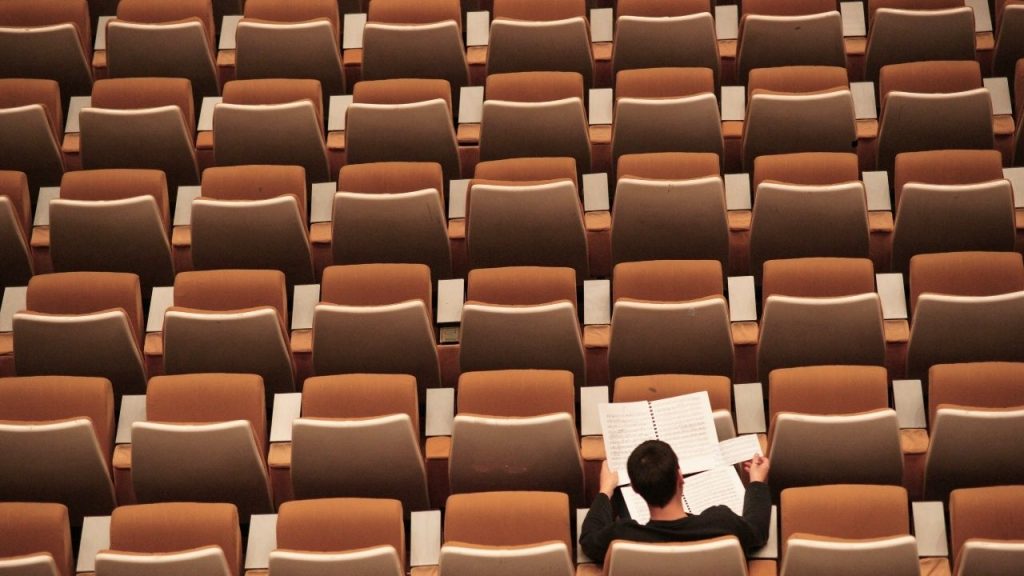 A photo from above a a lecture theatre seating area with a single student sat in one of the seats, studying some papers.