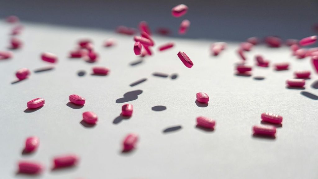 Pills being dropped onto a table with some of them captured in mid-air at the centre of the image.