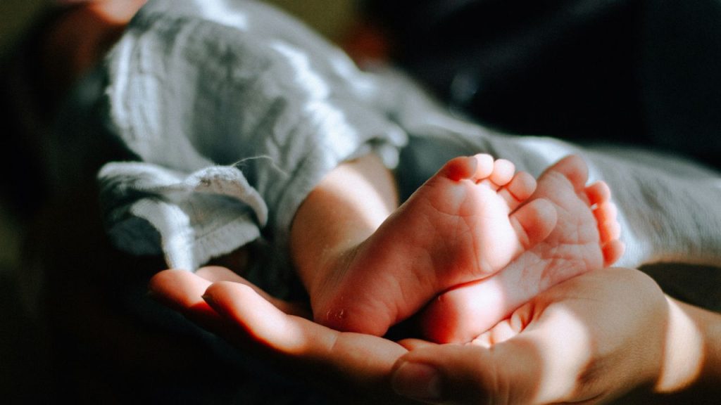 a close up of an adult hand cradling the feet of a baby.