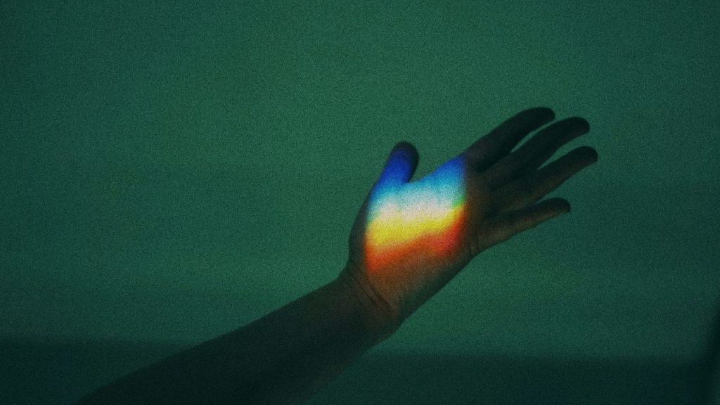 A photo of a hand with a rainbow of light projected on to the palm.
