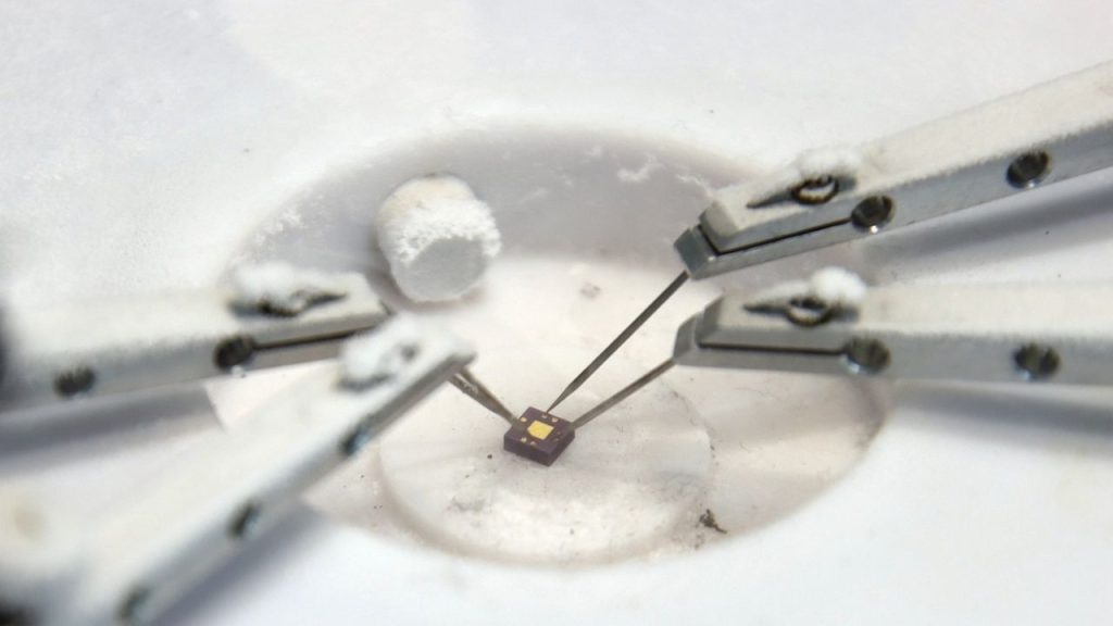 A macro photo of low temperature sensor testing on a graphene sensor chip. Lab utensils are connected to the tiny chip.