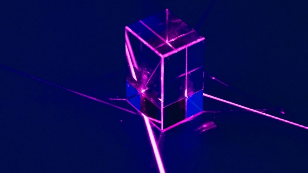 Pink laser beams intersecting a transparent cube against a deep-blue field, symbolising planqc’s neutral-atom quantum computer built from strontium qubits.