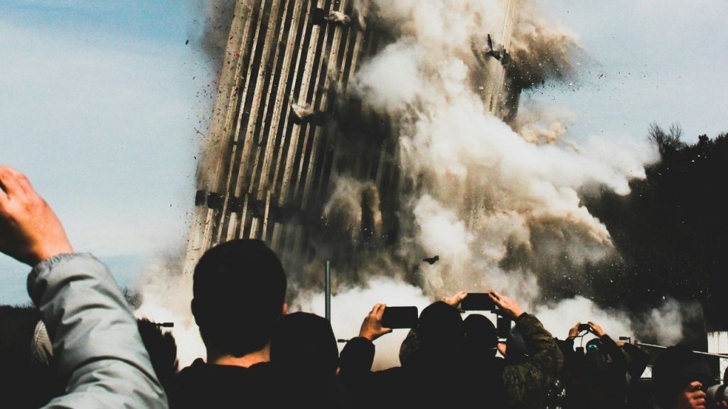 a building collapsing as part of a controlled demolition with a group of people filming it on their phones. The photo represents the misinformation and disinformation which Refute combats with its platform.