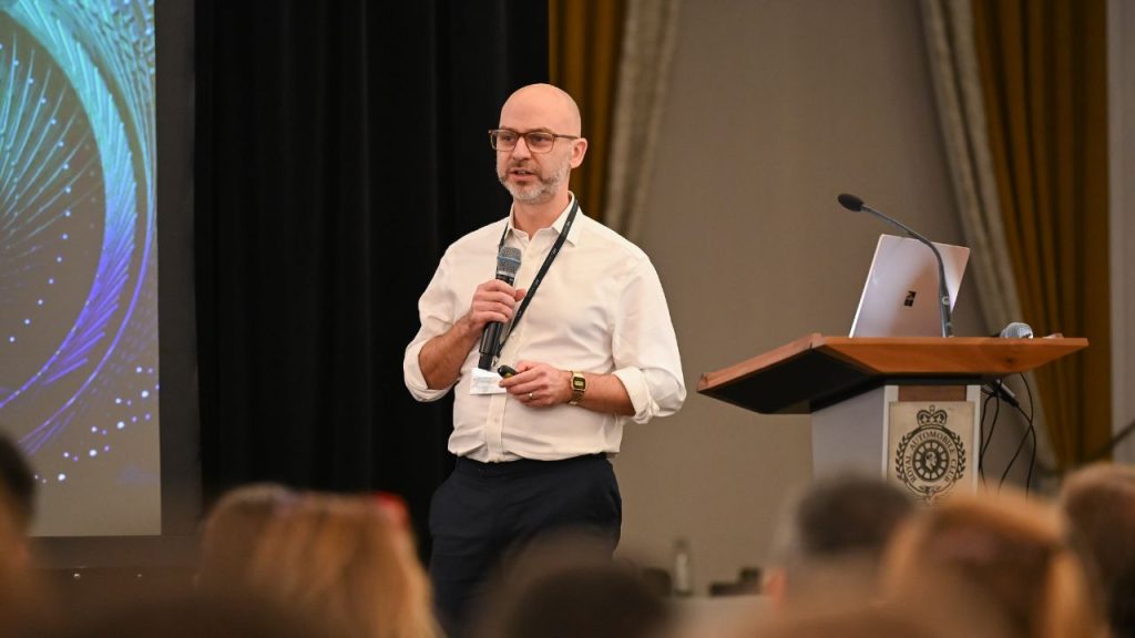 Riverlane CEO, Steve Brierley, speaking standing next to a lectern with a micrphone in hand while he speaks at an event.