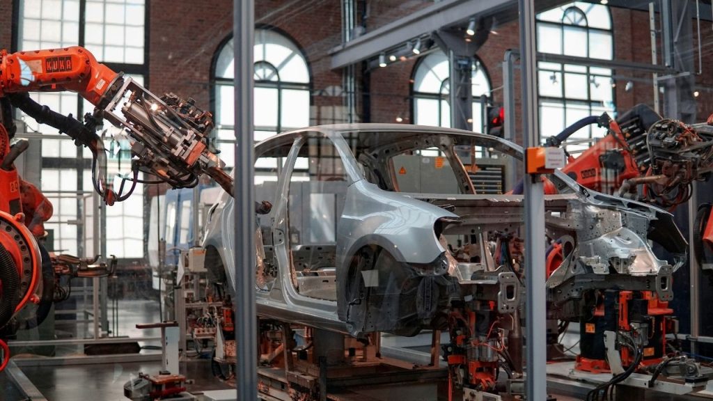a robotic arm working on constructing a car as part of an automotive construction line in a factory. The image is representative of the AI decision making platform which Secondmind has developed to to help car makers design betters cars, faster.
