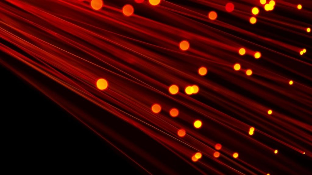 a close-up image of optical fibres which chows light shining through the tips of each fibre-optic cable. This is representative of the light-switching technology developed by Transdmode for telecoms operators.