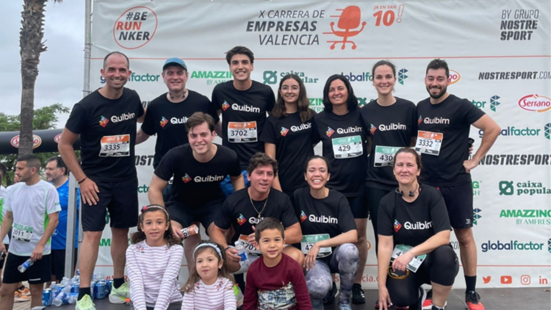 Ángel Alberich, co-founder and CEO of Quibim posing with his team at a charity running event. His children are also seated at the front of the stage.